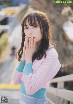 A woman in a pink sweater and blue skirt standing on a balcony.