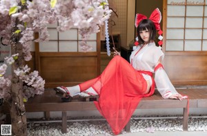 A woman in a red and white kimono sitting on a bench.