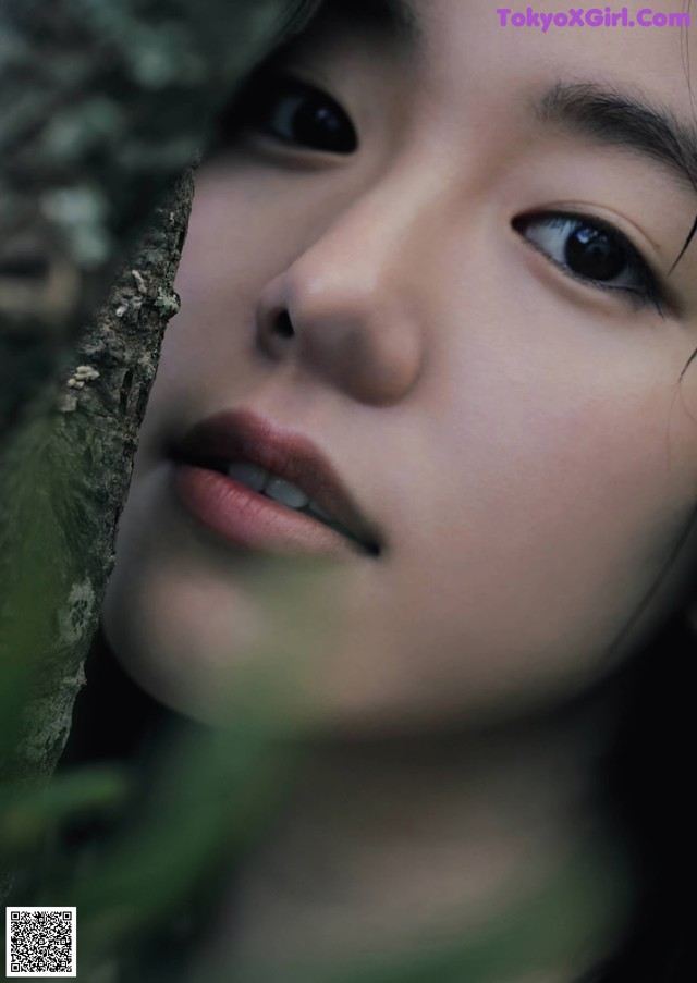 A close up of a woman's face peeking out from behind a tree.