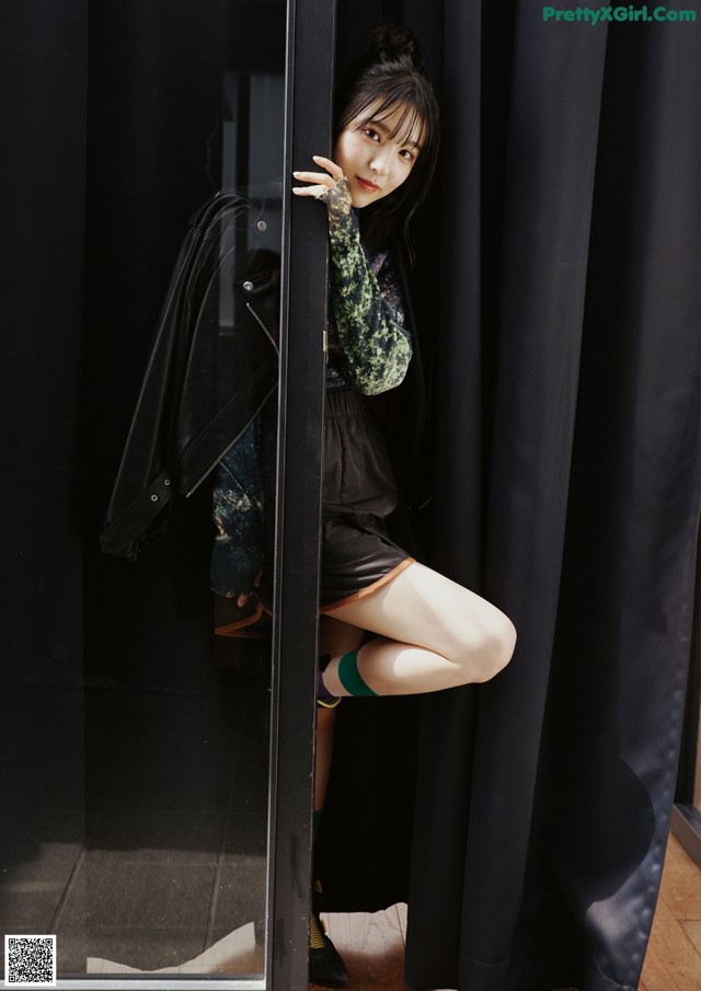 A woman leaning against a black curtain in a room.