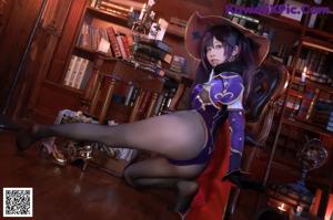 A woman in a witch costume sitting on a chair in front of a bookcase.