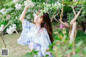 A woman in a blue and white kimono crouching down in the grass.
