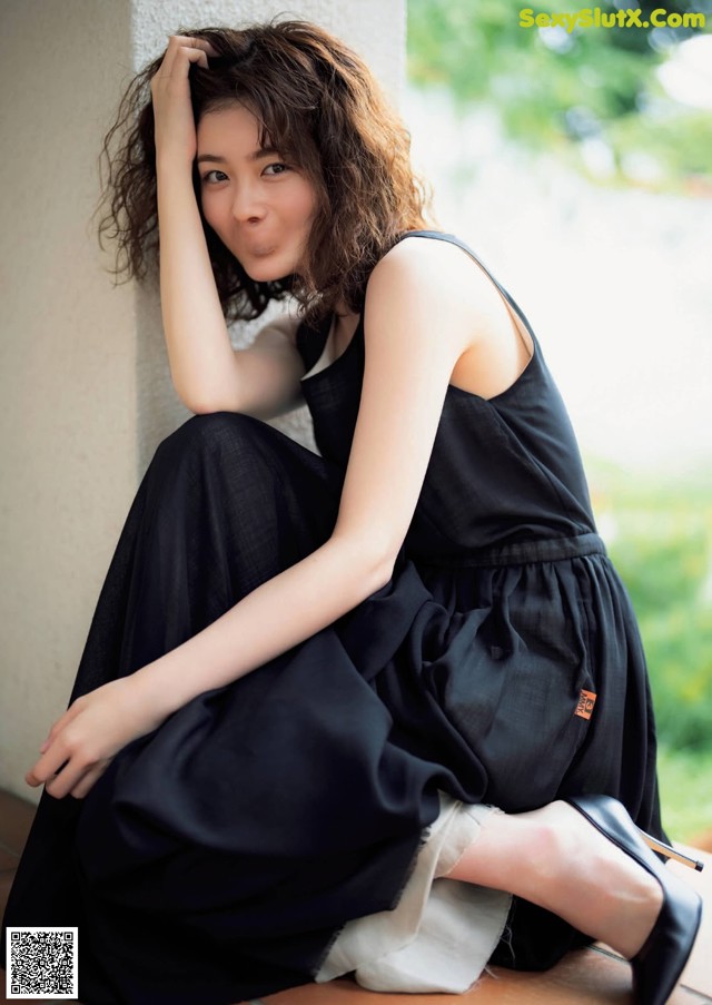 A woman in a black dress sitting on the ground.