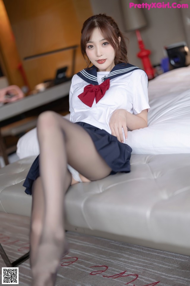 A woman in a school uniform sitting on a bed.