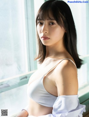 A woman in a white bra top and plaid skirt posing by a window.