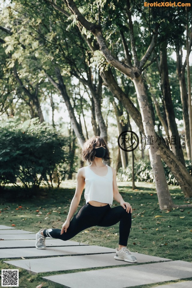 A woman wearing a face mask doing yoga in a park.