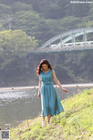 A woman in a blue dress standing by a river.