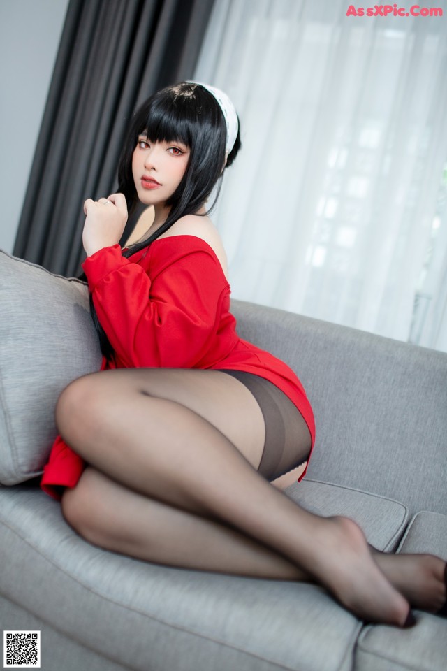 A woman in a red dress sitting on a gray couch.