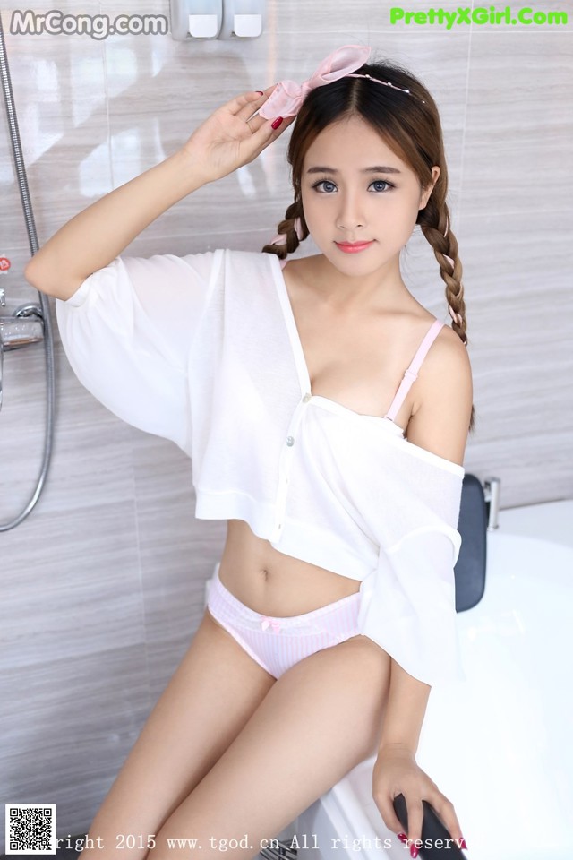 A woman in a white shirt and pink panties sitting in a bathtub.