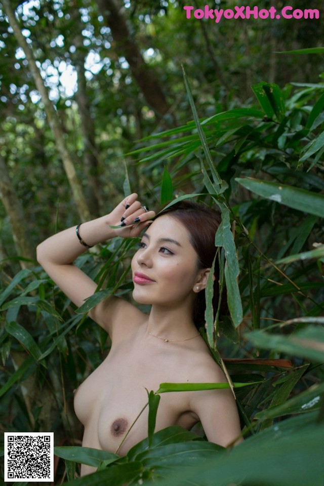 A naked woman standing in the middle of a forest.