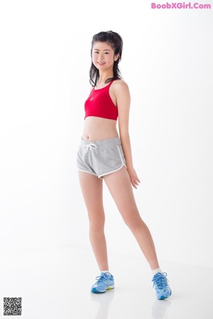 A woman in a red top and gray shorts leaning against a wall.