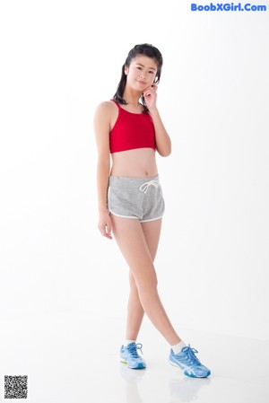 A woman in a red top and gray shorts posing for a picture.