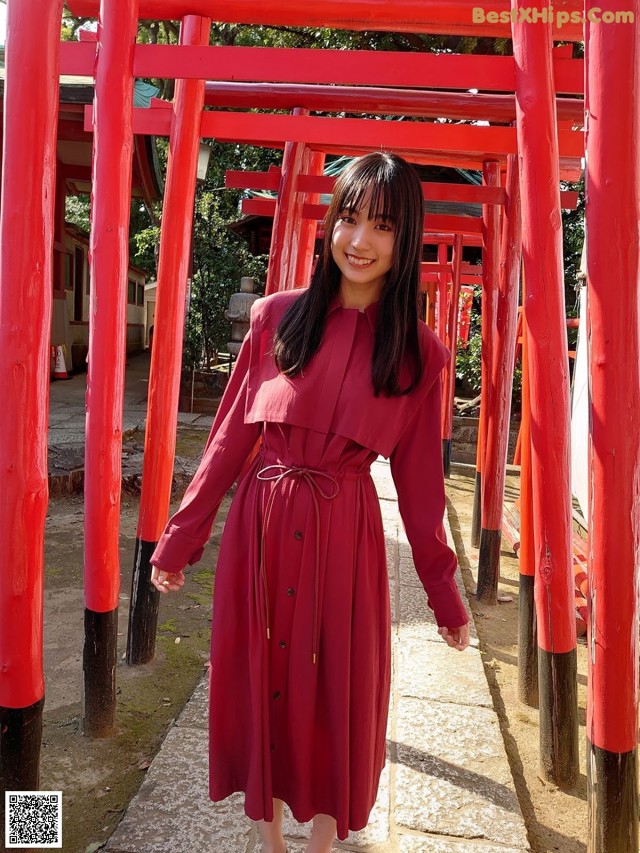 A woman in a red dress standing in front of red torii gates.