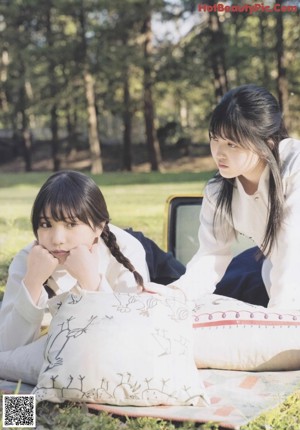 A couple of girls laying on top of a blanket in the grass.