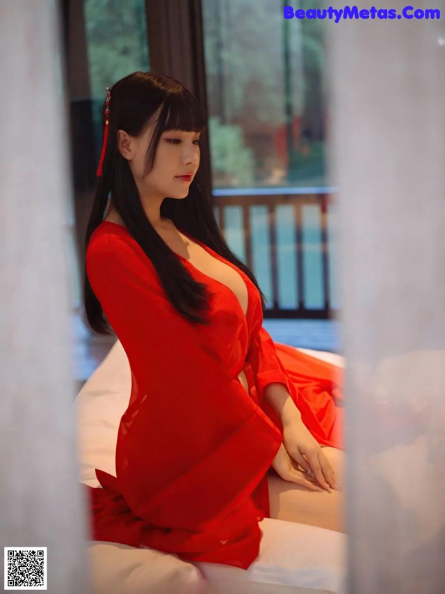 A woman in a red dress sitting on a bed.