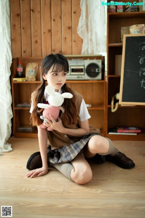 A naked woman sitting on the floor next to a teddy bear.