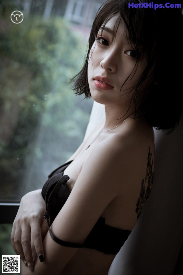 A woman in a black bra sitting by a window.