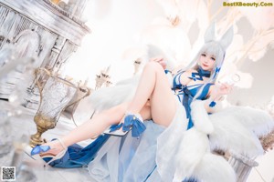 A woman in a blue and white outfit sitting on a white couch.