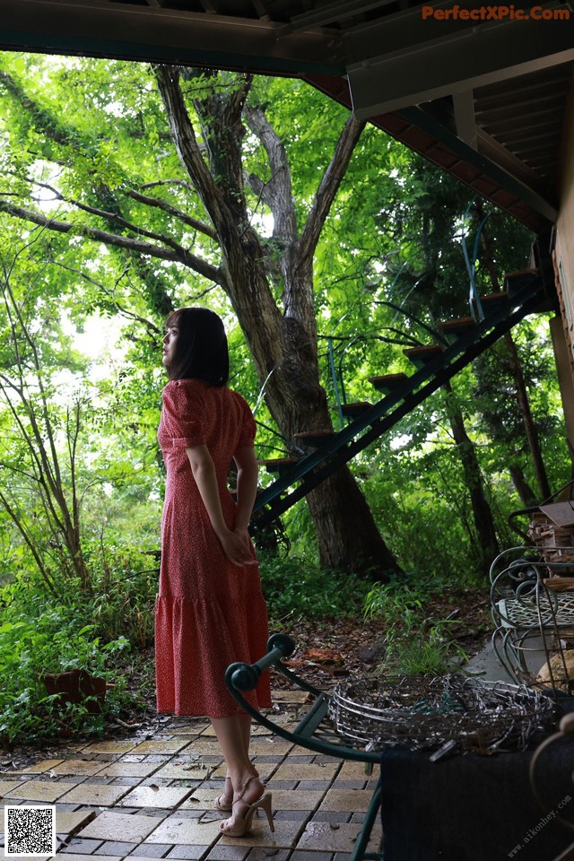 A woman in a red dress standing in front of a tree.