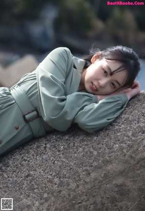 A woman in a green dress sitting on a stone wall.
