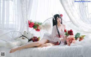 A woman in a pink robe sitting on a bed.