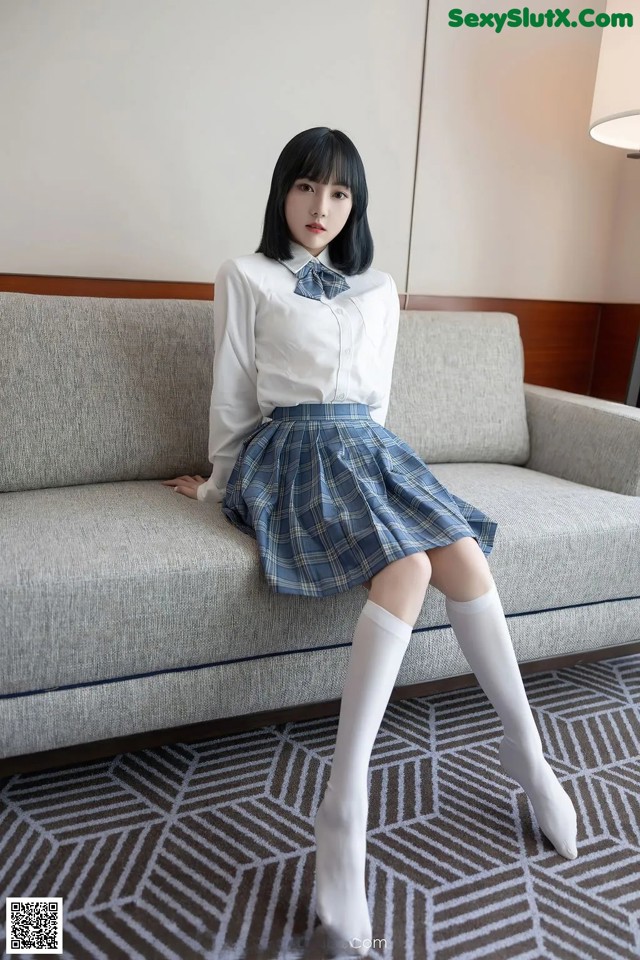 A woman in a school uniform sitting on a couch.