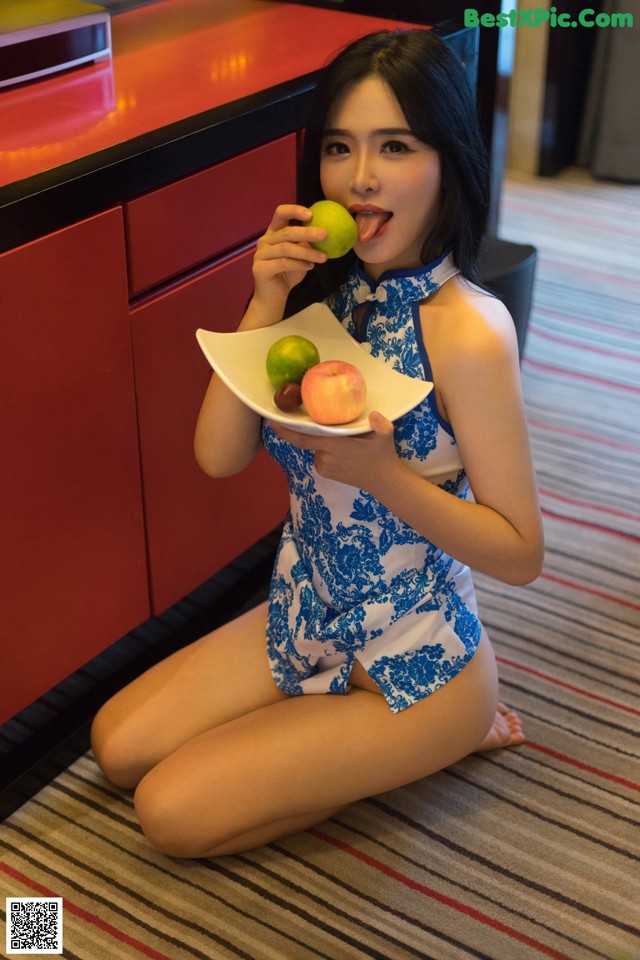 A woman in a blue and white dress holding a plate of fruit.