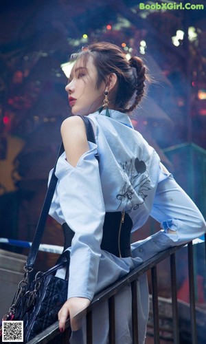 A woman in a white shirt and black skirt leaning against a fence.