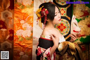 A woman in a kimono sitting on a red couch holding a fan.