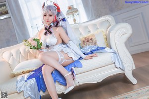 A woman in a white and blue outfit sitting on a bed.