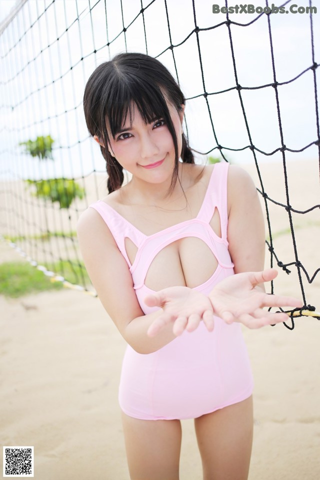 A woman in a pink bathing suit standing next to a volleyball net.