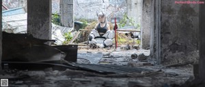 A woman in a black top and white pants standing in an abandoned building.