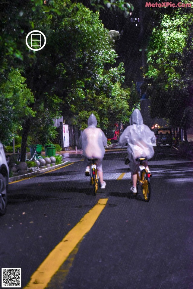 A couple of people riding bikes down a street in the rain.