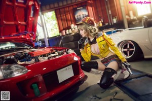 A woman in a yellow jacket and black gloves sitting next to a white car.