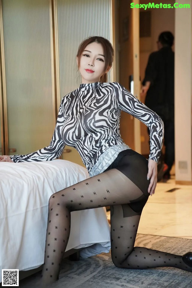 A woman in a zebra print top and black tights posing on a bed.