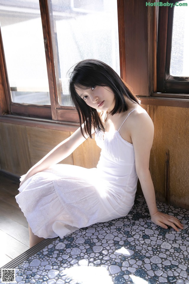 A woman in a white dress sitting on a window sill.