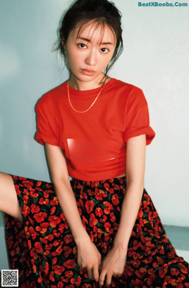 A woman wearing a red shirt and a floral skirt.