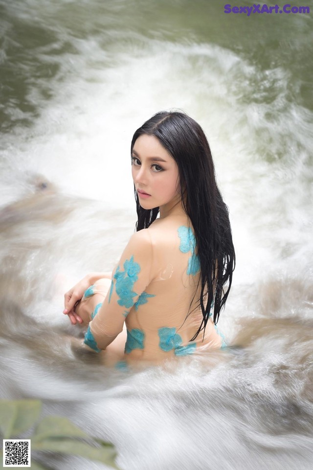 A woman in a blue bikini sitting in a river.