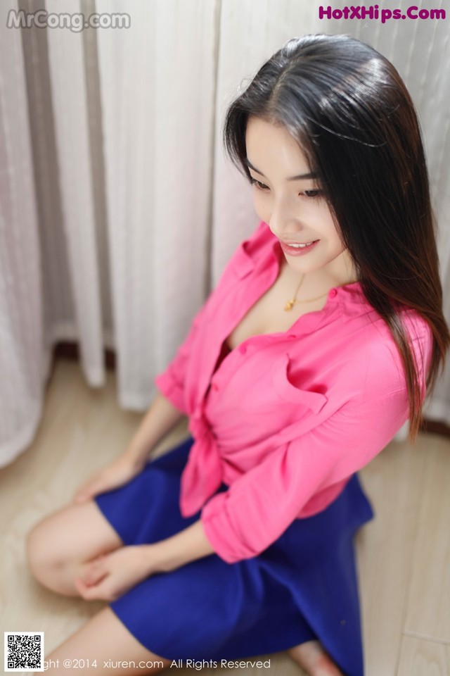 A woman in a pink shirt and blue skirt sitting on the floor.