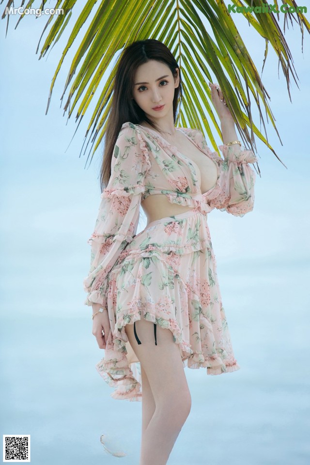 A woman in a pink dress standing next to a palm tree.