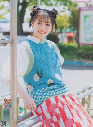 A young woman sitting on the ground wearing a colorful shirt and skirt.