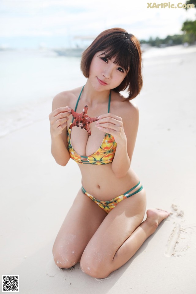 A woman in a bikini holding a starfish on the beach.