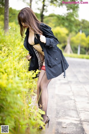 A woman in a black jacket and red stockings is posing in the grass.