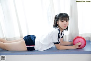 A young girl holding a red dumbbell on a blue mat.