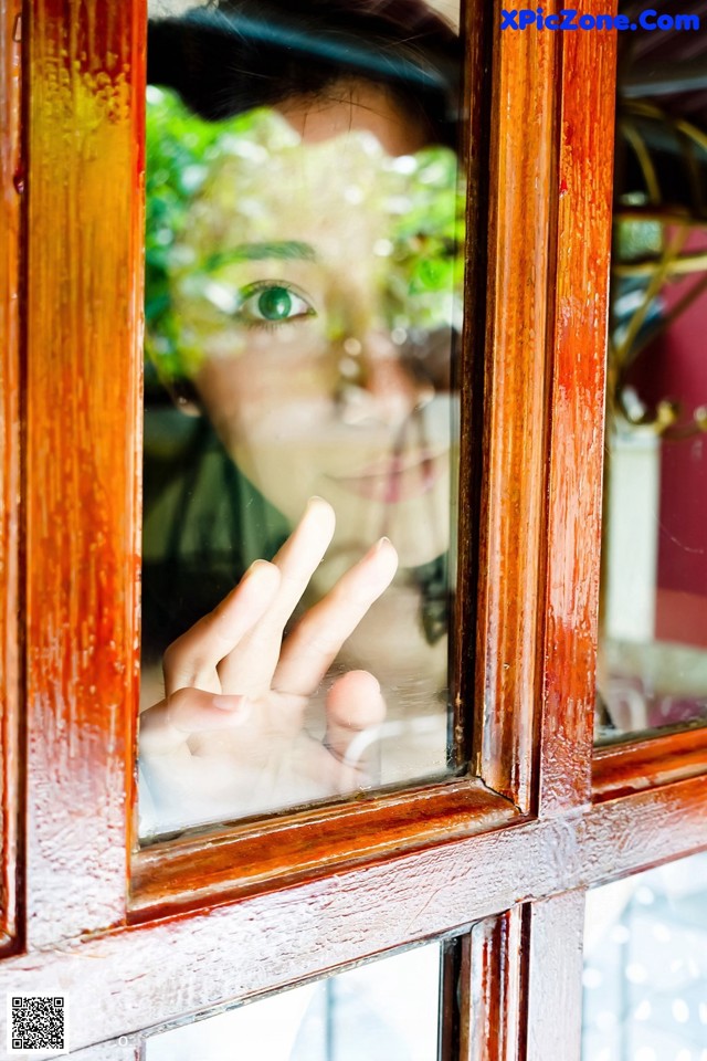 A woman is looking out of a window with her hand up.